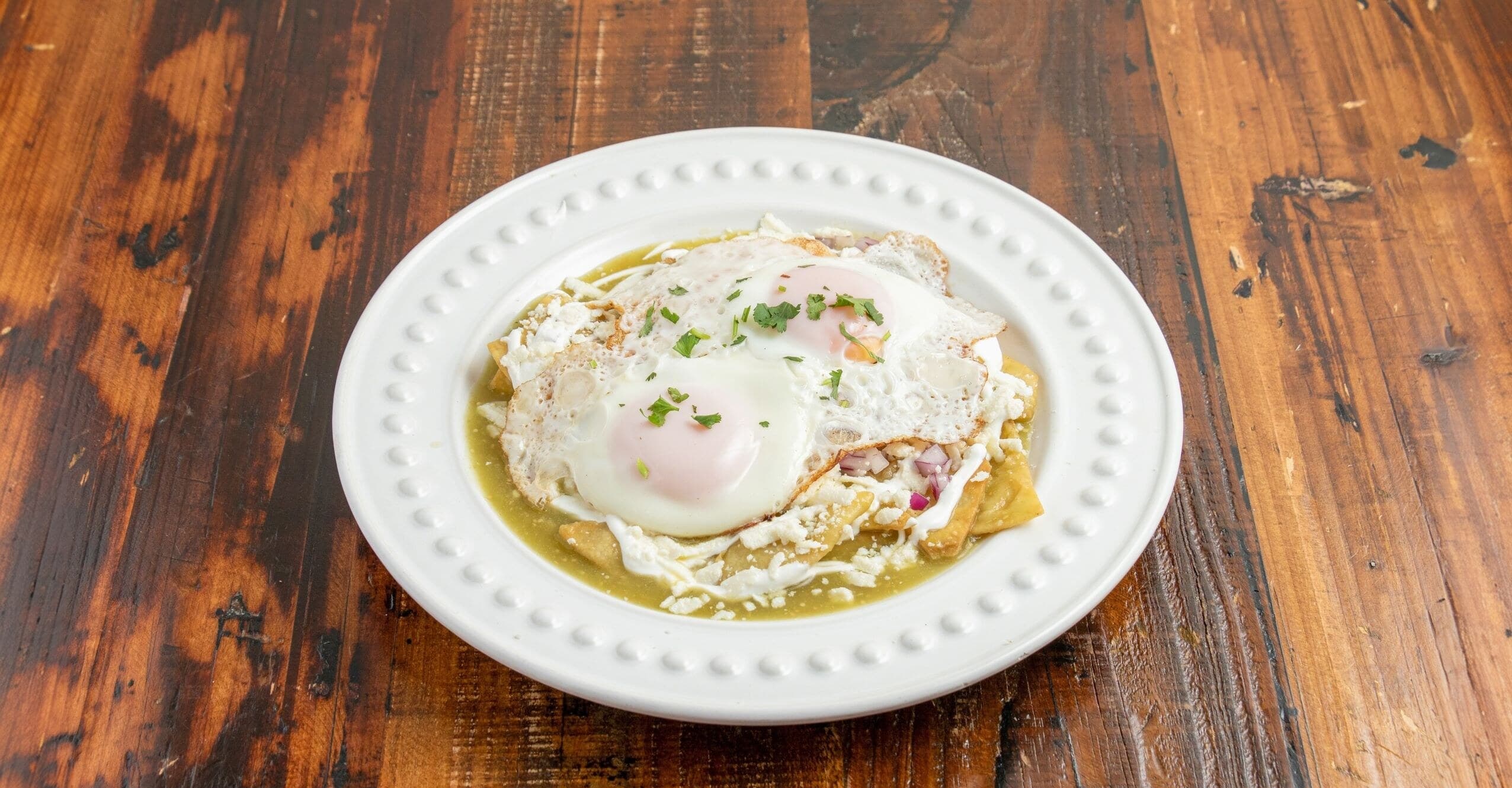 Chilaquiles verdes topped with two eggs, crema, queso fresco, onion, and cilantro