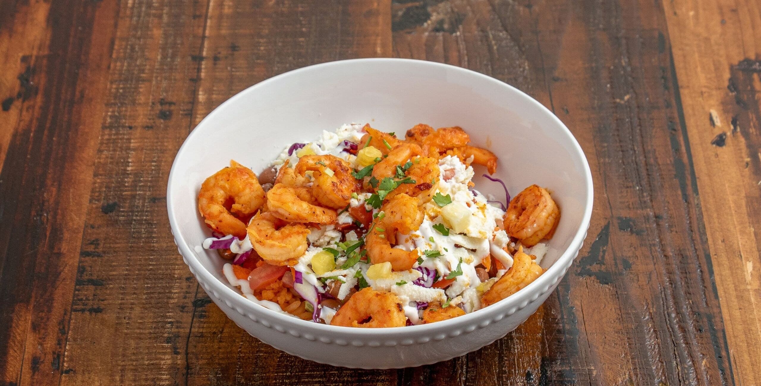 Shrimp bowl with grilled shrimp, rice, cabbage, tomato, pineapple, crema, and cheese