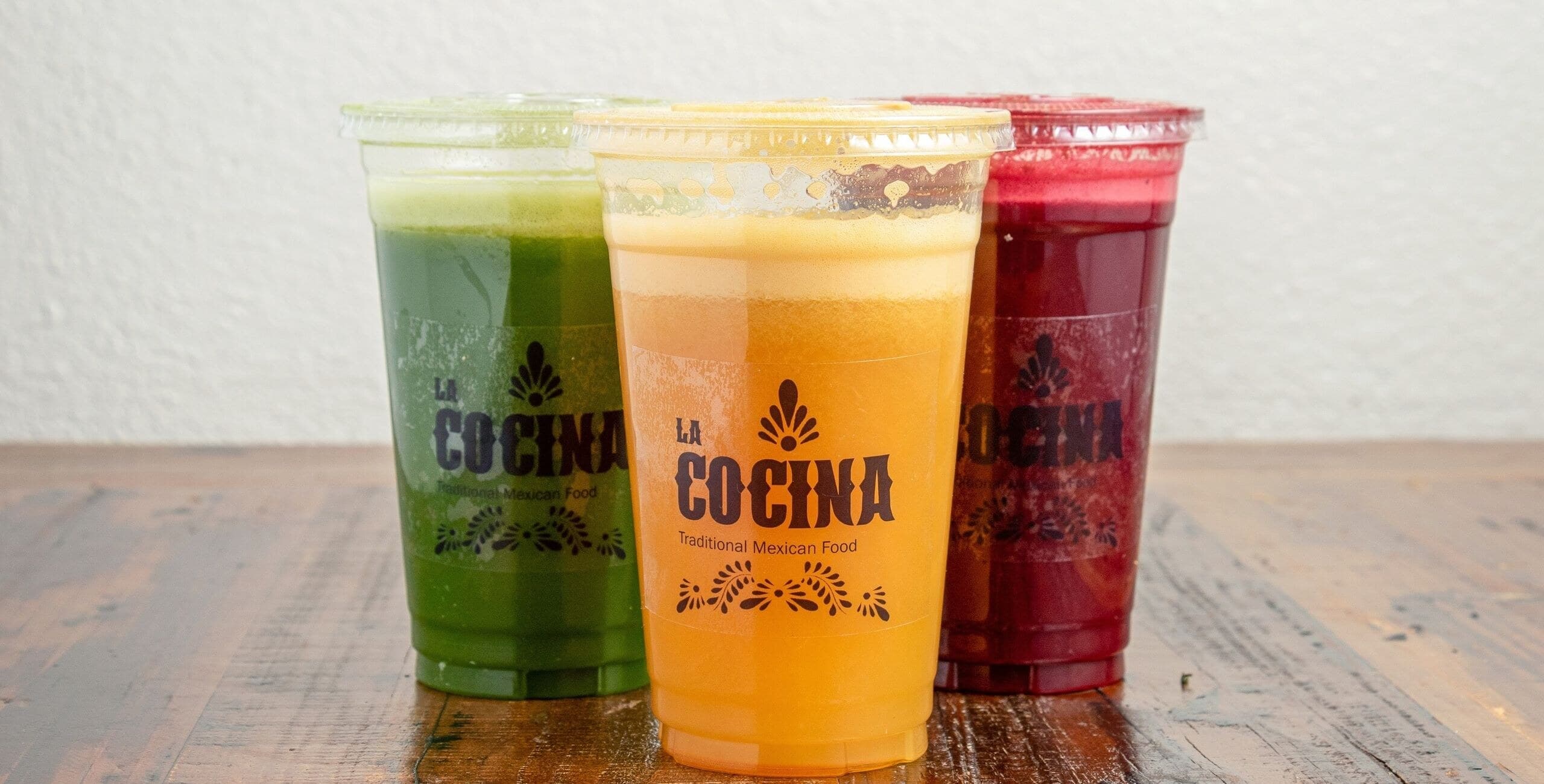 Three fresh La Cocina juices in green, orange, and deep red, served in branded cups
